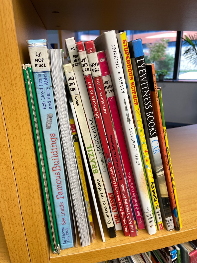 nonfiction library books on a shelf, some upside down
