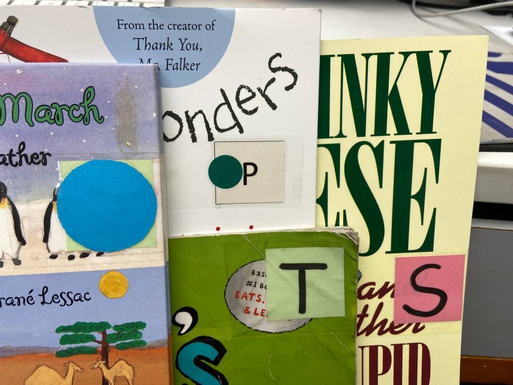 four books with large labels in different colors showing different letters